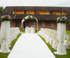 Cerimonia di nozze all'aperto con arco di fiori e alti vasi sulla guida